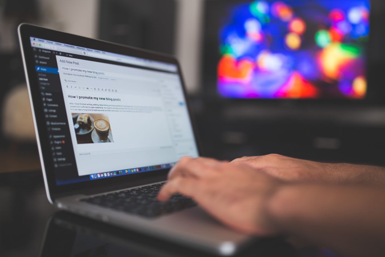Home Hands typing on a laptop with a blog post visible, cozy indoor setting with colorful screen in background.