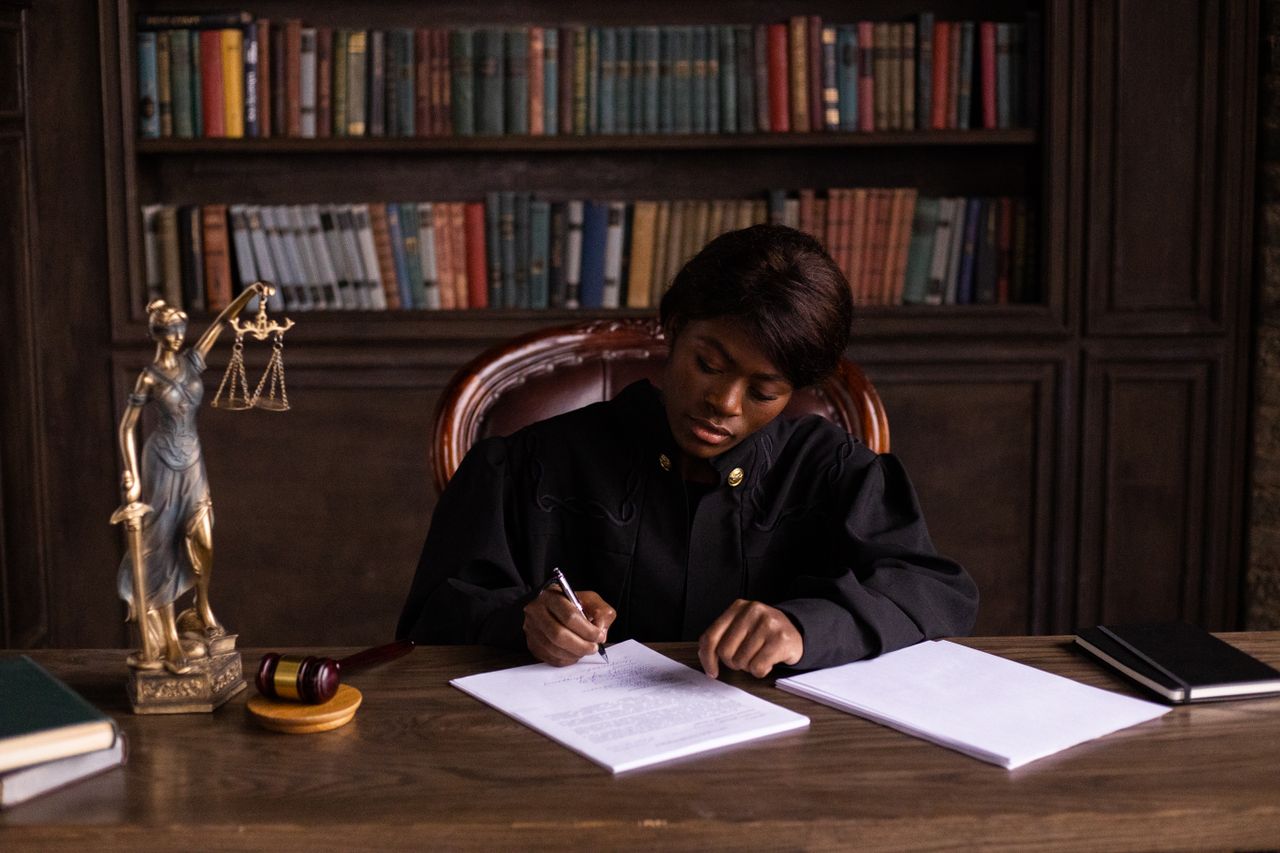 Mastering the First Impression: Your intriguing post title goes here A judge in robes writing on a document at a desk in an office library with law books.